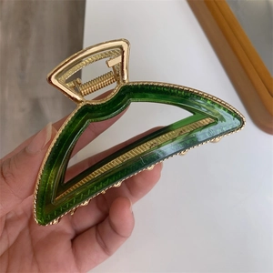 Detail of emerald green acetate hair claw clip with golden metal frame and bead texture