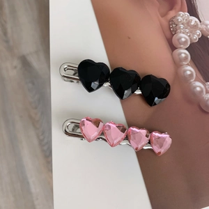 Vista dettagliata dei fermagli per capelli con cristalli a forma di cuore rosa e neri su metallo