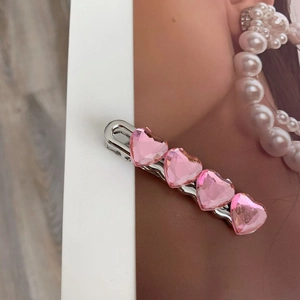 Dettaglio di un fermaglio argentato con quattro cristalli a cuore rosa sfaccettati
