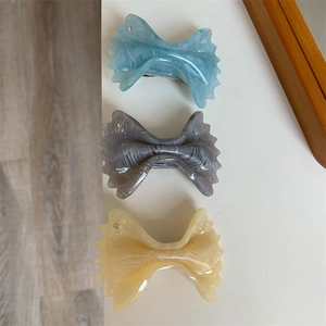Three acetate bow hair clips in blue, marble, and cream yellow with small rhinestone accents