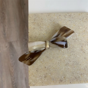 Détail de la pince à cheveux nœud en acétate écaille avec logo doré sur fond de pierre