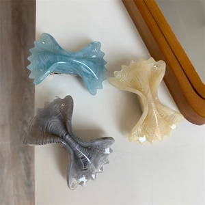 Detail of bow-shaped acetate hair clips featuring marble texture and small rhinestone