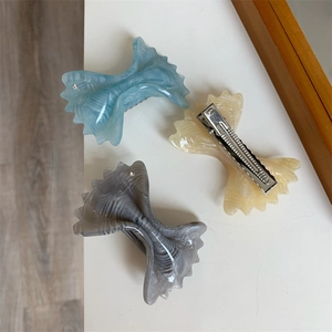 Detail of bow-shaped acetate hair clips in blue, beige, and grey with rhinestone accents
