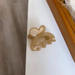 Detail of beige resin hair claw with golden Handmade lettering and floral petal shape