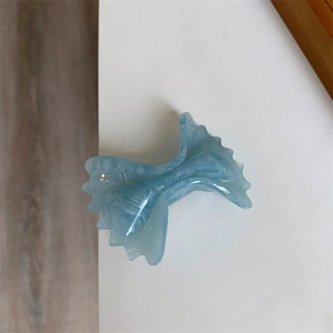 Detailed macro view of light blue acetate bow hair claw with marble texture and rhinestone