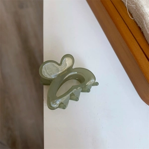 Macro view of butterfly hair clip in sage green resin with golden sunshine text