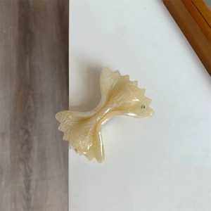 Close-up of cream acetate bow hair clip with marble texture and small rhinestone detail