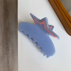 Detailed close-up of a blue acetate hair claw clip with inlaid pink star rhinestones