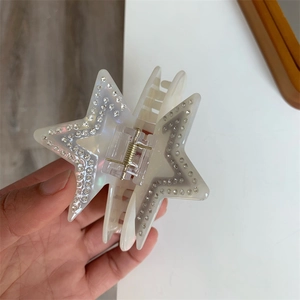 Close-up of iridescent cream acetate star hair claw clip with rhinestones and gold spring