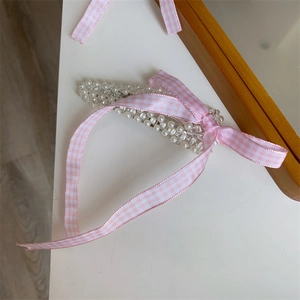 Detail einer Haarspange mit rosa karierter Schleife, weißen Kunstperlen und Perlen