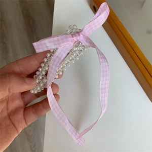 Detail einer perlenbesetzten Haarspange mit einer rosa karierten Schleife für Frisuren