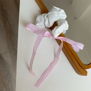 Detail von rosa karierter Bandschleife und weißem Rüschen-Haargummi auf Holzrahmen