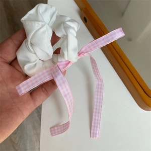 Detailansicht eines weißen Scrunchies mit einer rosa-weiß karierten Schleife aus Seide