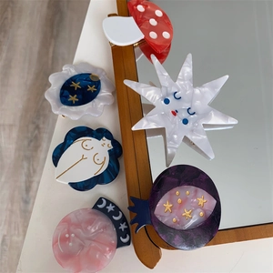 Artistic cellulose acetate hair clips with mushroom and star designs on a mirror surface