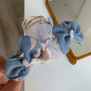 Détail de la pince à cheveux avec nœud floral bleu en tissu élégant et plastique transparent