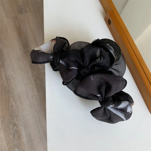 Détail d'une pince à cheveux avec nœud en maille noire et motifs floraux blancs