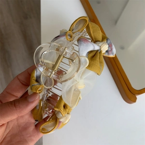 Détail d'une grande pince à cheveux avec un nœud en tissu jaune et motif floral