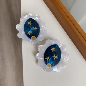 Close-up of white petal acetate earrings with blue starry night theme and gold moon motifs