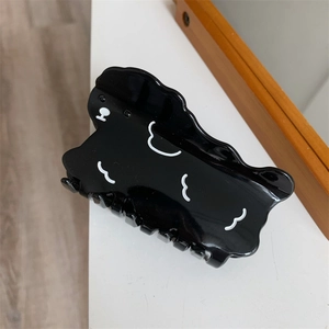Detail shot of a black acetate hair claw clip with white cloud pattern on a white desk