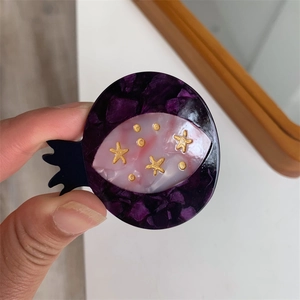 Macro view of handmade acetate pomegranate hair clip with purple floral and star patterns