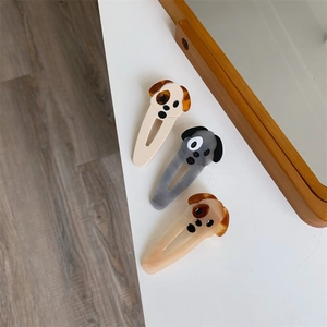 Close-up of three cute squinting dog hair clips in cream, grey, and coffee colors