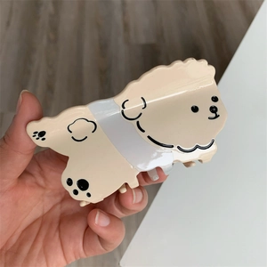 Detalle de pinza para el pelo de acetato con forma de caniche beige sujeta a mano