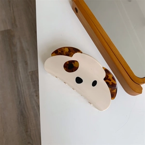 Detail view of a cream and tortoiseshell acetate puppy dog hair claw clip on a white table