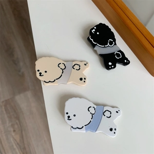 Three cute cartoon poodle hair clips in beige, black, and white on a clean table