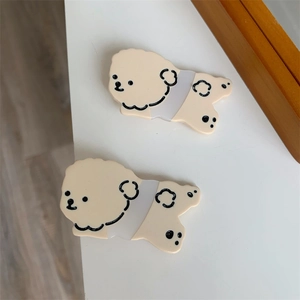 Close-up of two cute cream-colored acrylic cartoon puppy hair clips on a white surface