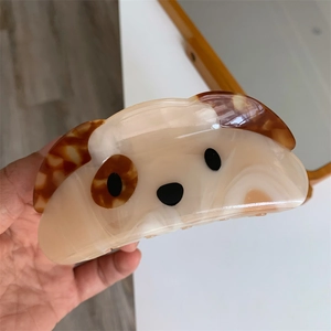 Handheld view of a squinting dog hair claw clip made of beige and brown acetate material