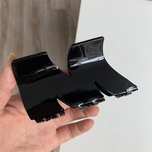 Detail of a large black M-shaped acetate hair claw clip with a glossy finish and metal spring