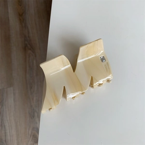 Detail view of cream acetate hair claw clip featuring inlaid rhinestone and letter M