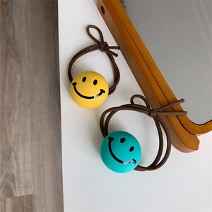 Close-up of yellow and blue smiley face elastic hair ties on a minimalist white table