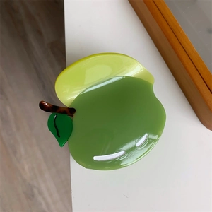 Vista macro di un fermaglio per capelli a forma di mela verde lucida con dettagli di foglie