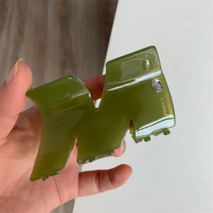 Detailed side view of olive green acetate hair claw with rhinestone and gold lettering