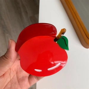 Dettaglio di una molletta per capelli a forma di mela rossa con foglie verdi e stelo