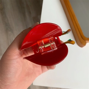 Dettaglio di un fermaglio per capelli in acrilico rosso lucido con molla in metallo oro