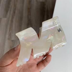 Close-up of pearl white acetate hair claw clip with crystal letter M rhinestone detail