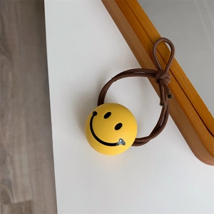 Detailed shot of yellow smiley face charm on a brown multi-strand elastic hair tie