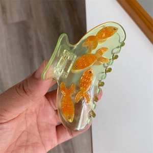 Détail d'une pince à cheveux vert translucide ornée de petits poissons rouges en résine