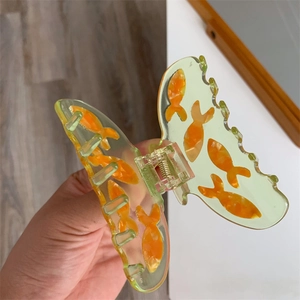 Gros plan d'une pince à cheveux papillon verte translucide avec motif de poisson rouge