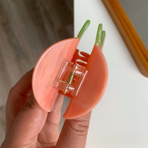 Dettaglio della pinza per capelli a forma di pesca in acetato rosa marmorizzato e verde