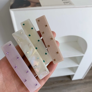 Close-up of four colorful acetate hair clips with inlaid rhinestones held in hand