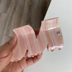 Detail of pink marble acetate hair claw clip with crystal inlay and gold letter engraving