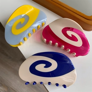 Top view of three colorful spiral patterned hair claws on a clean white desk