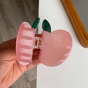 Dettaglio di un fermaglio per capelli a forma di pesca rosa con foglie verdi in acrilico