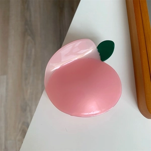 Dettaglio ravvicinato di una molletta per capelli a forma di pesca rosa con foglia verde