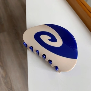 Detail view of a swirl patterned hair claw clip in deep blue and cream white acetate material