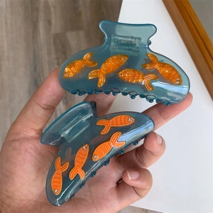 Détail d'une pince à cheveux bleue avec motifs de poissons oranges et petits cristaux