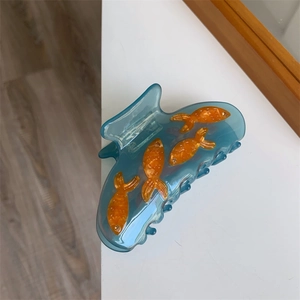 Détail d'une pince à cheveux en acrylique bleu avec motif poisson sur fond blanc